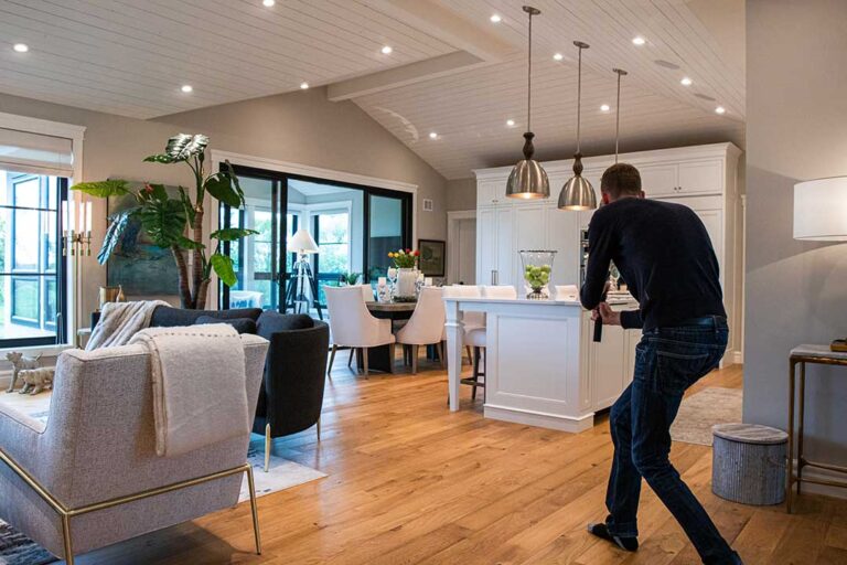 A home inspector examines a home's electrical panel with a flashlight while a homebuyer observes nearby.
